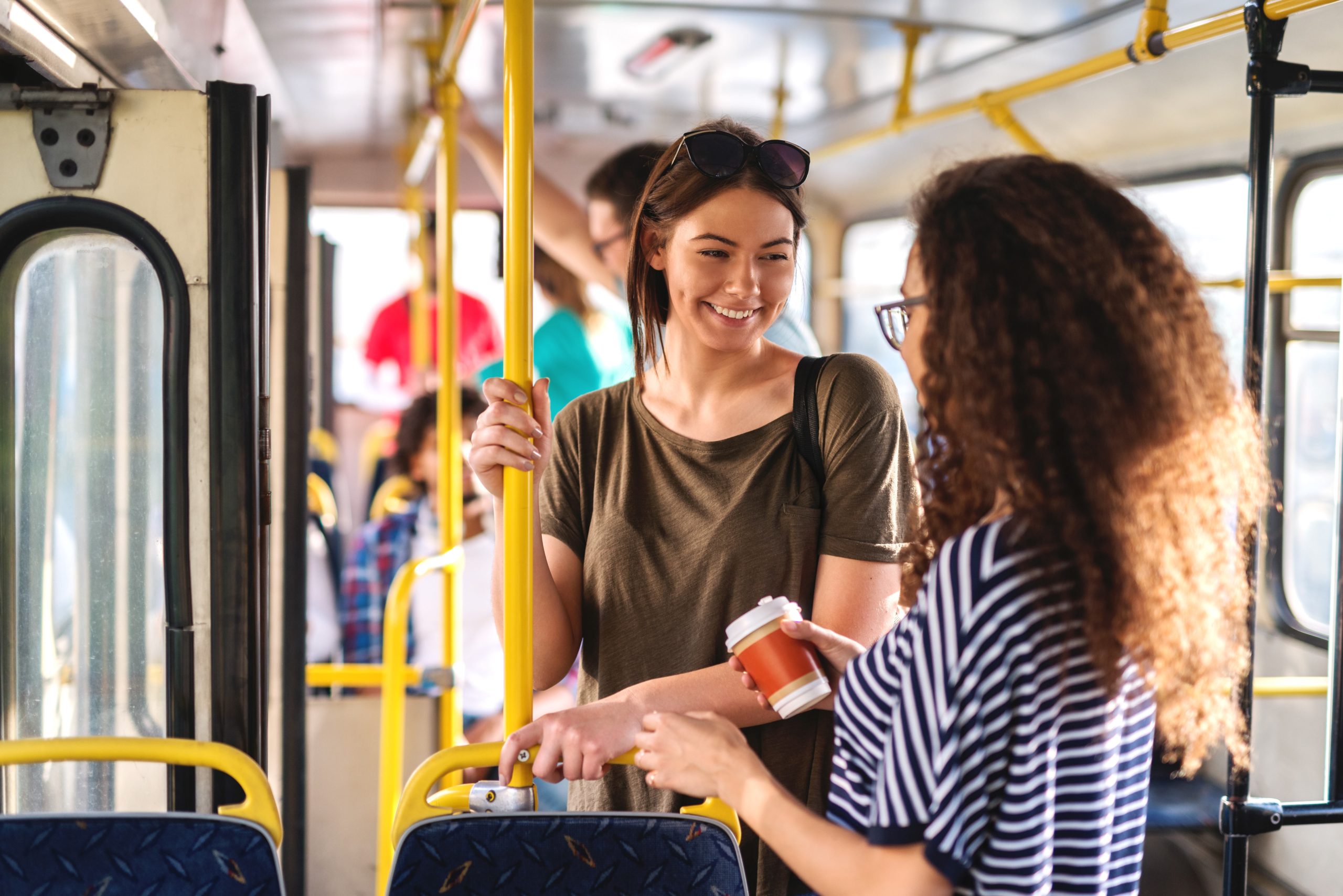 Two people are standing on a bus enjoying friendly conversation and coffee.